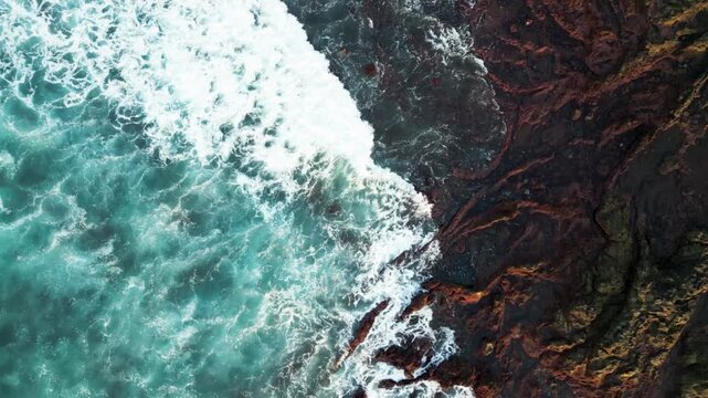 Aerial view of ocean waves crashing on rugged rocky shoreline