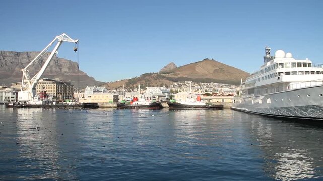 Large white yacht docked at harbor with crane and boats