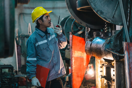 Worker factory helmet radio machinery inspection industrial uniform clipboard safety, male worker wearing yellow helmet using radio during factory machinery inspection with clipboard