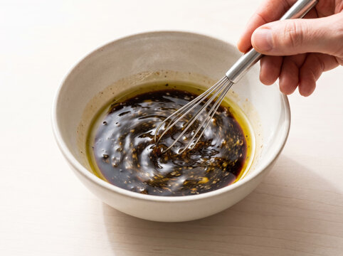 Whisking dark balsamic glaze with olive oil in a ceramic bowl