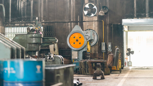 Industrial workshop machinery factory equipment metal tool warehouse ventilation door concrete interior with heavy press, barrel, fan, hoist, pipe, cluttered floor, and worn manufacturing workspace