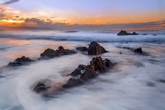 Stunning long exposure sunset at Barrika beach showing silk water flowing between geological flysch rock formations on the Basque coast of Spain