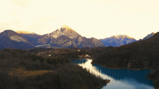 Horizontal 4K 24fps aerial drone video flying slowly forward over the turquoise water of Lake Verzegnis, Italy, pointing towards a sunlit mountain peak during a cold winter day