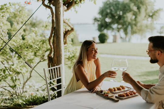 Couple enjoys food and drinks at outdoor table near water during afternoon