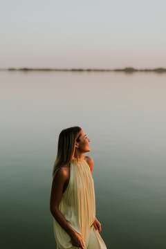 Woman stands by lake during sunset looking towards water and horizon