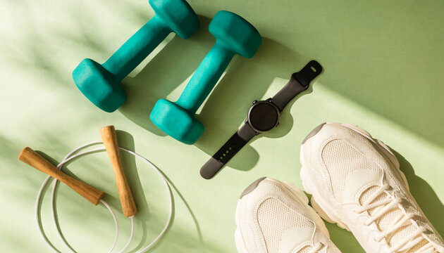 Fitness equipment and dumbbells on green background. Workout gear for home exercise routine.