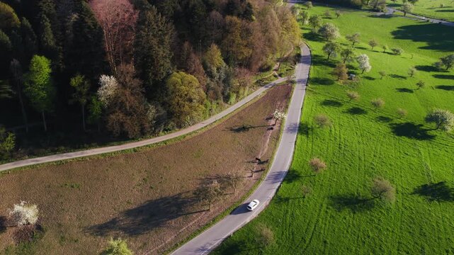 Aerial bird's-eye view of an idyllic rural landscape with a white car driving on a scenic road 