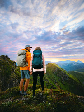 Couple with backpacks travel in Norway friends hiking together in Lofoten islands, man and woman enjoy sunset view on adventure summer romantic vacation tour healthy lifestyle activity family holidays