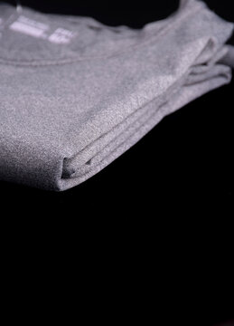 Folded gray heather T-shirt, close-up on the dry-fit fabric at the fold, portrait orientation, black background.