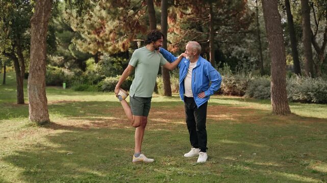 Senior father and adult son stretching after sport training session at park 