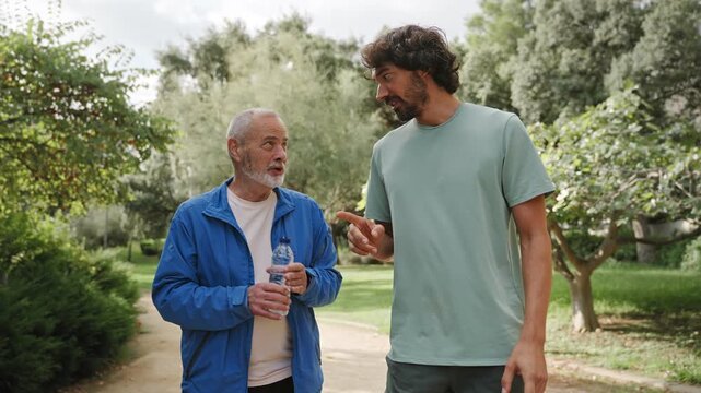 Senior father walking and talking with his son, public, enjoying conversation after doing sport