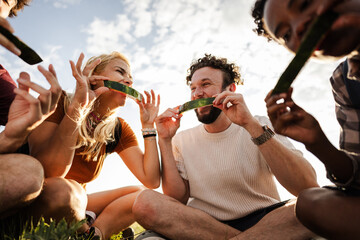 Fototapeta premium Eating Watermelon Together With Friends at Sunset During a Gathering in a Green Field