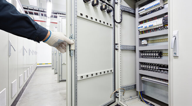 Electrician's hand opening an electrical control panel in a modern facility