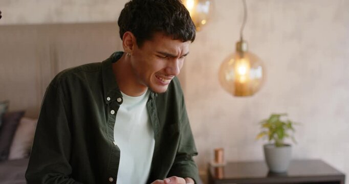 African American man clutching abdomen after sudden pain, grimacing on bed wearing dark green shirt