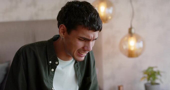 African American man grimacing from sudden pain, leaning on bed, pressing abdomen by pendant lights