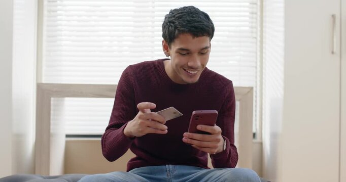 African American man sitting on tufted seat in maroon sweater glancing at phone, checking card