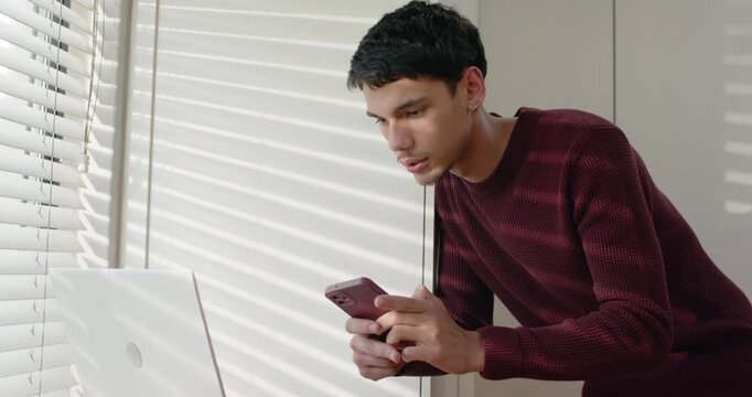 Adult African man leaning on sill reading pinkphone speaking responding typing laptop, copy space