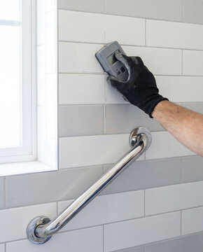 Contractor using stud finder on bathroom wall before grab rail installation
