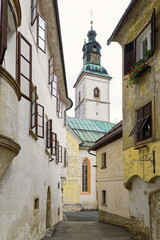 Fototapeta premium St.Jacob church south side and belfry jutting into the overcast sky, seen through buildings on Mestni trg and Cankarjev trg. Skofja Loka-Slovenia-156