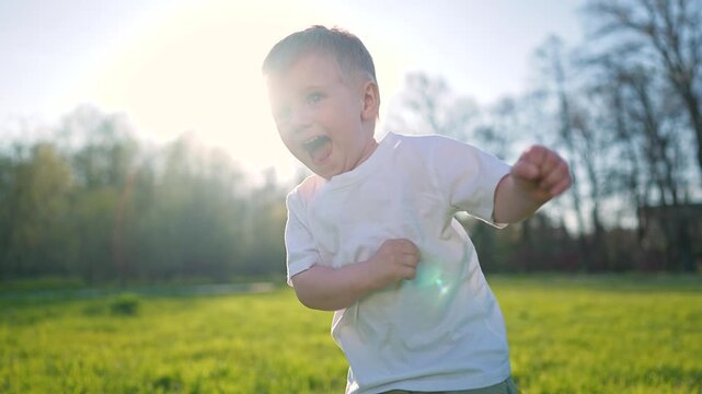 Happy toddler smiles while walking in grass. Child explores sunny outdoor space. Toddler enjoys playful moment in nature. Kid walks with joy, toddler steps show fun, child grows through active play.