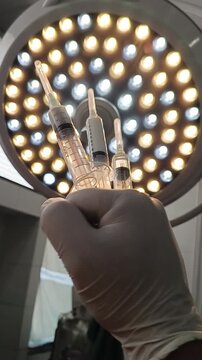 Hand in glove holding three prepared medication syringes in front of surgical light