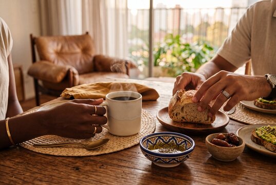 Close-up of a diverse couple enjoying a healthy breakfast with steaming coffee and fresh sourdough bread in a sunlit modern apartment