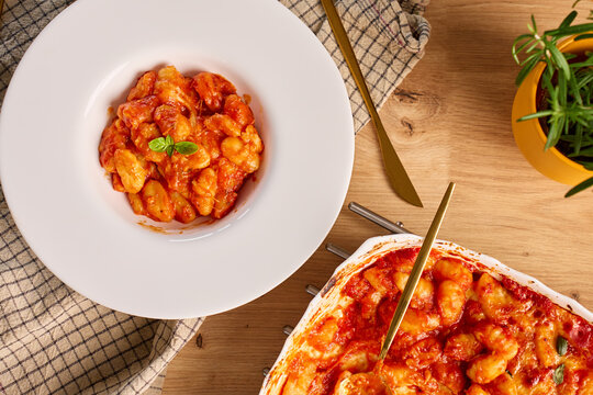 Gnocchi with tomato sauce, melted cheese and basil served on plate beside ceramic baking dish
