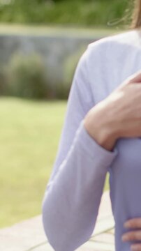 Vertical video: Camera panning, woman placing hand on chest on bench, lilac top, copy space
