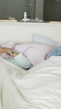Vertical video: Waking woman in mint top reaching across bed in bedroom, comforting man in blue top