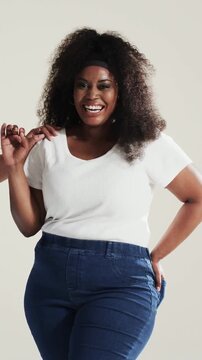 Vertical video: Smiling model posing in studio with co-model entering, wearing white top, jeans