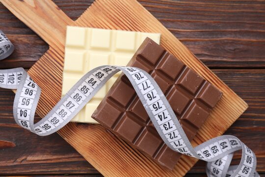 Measuring tape and chocolate bars on wooden table, top view