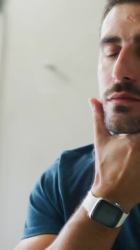 Vertical video: Facing mirror man in tee and white watch in vanity feeling jaw neck checking beard