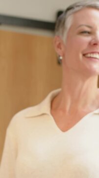 Vertical video: Smiling mature woman gesturing, laughing after prompt at home, in sweater, books