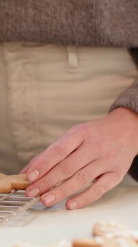 Vertical video: Placing cookies on wire rack for cooling in kitchen, baker smiling in brown knit