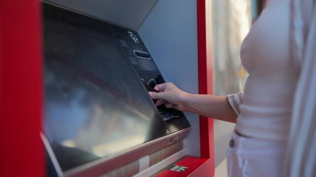 Close-up of woman inserting bank card into outdoor ATM and entering PIN code. Secure cash withdrawal, banking services, financial transaction and modern payment technology concept