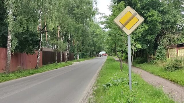 Crossed-out priority road sign along a quiet tree lined street, road safety, traffic navigation, suburban transport, travel concept.