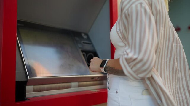 Unrecognizable woman stand outdoors and using an atm, inserting card, enter pin on touchscreen, and completing financial transaction to withdraw cash from machine