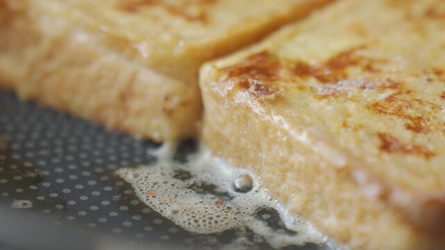 French toast frying in pan with browned bread slices and bubbling butter