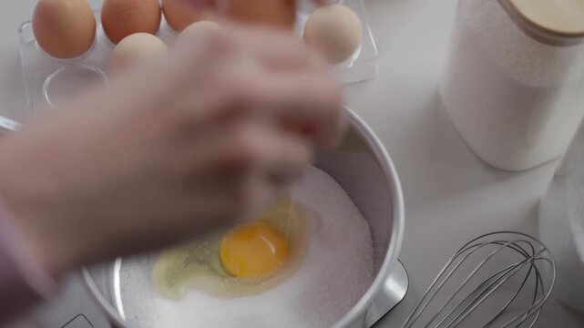 Cracking two eggs into sugar in saucepan, with egg tray, whisk and jars