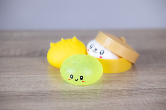 Closeup view of small round squishy toy with smiling face and blushed cheeks on light wood surface, soft blur behind it, translucent green tones, playful product style, bright cheerful colors