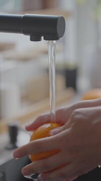 Hands wash orange under running water at kitchen sink