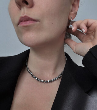 Stylish woman wearing hematite stone choker necklace and silver earrings in black blazer close up. Elegant dark grey beaded jewelry set. Modern female portrait, fashion accessories concept.