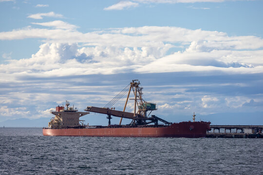 Bulk Carrier Cargo Ship Docked at Port With Conveyors Under Dramatic Cloud Sky in Tsawwassen