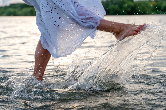 Woman splashes water while walking at a lake during daylight with trees in the background