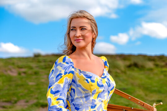 Woman stands in field holding an instrument on a sunny day with clouds in the sky