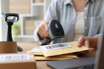Fototapeta premium Post office worker with scanner reading barcode at desk indoors, closeup