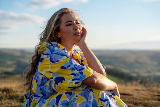 Woman sitting on a hillside looking at the landscape while wearing a colorful dress during daylight