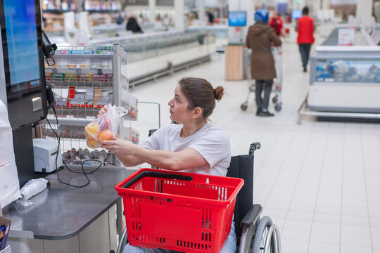 A Caucasian woman in a wheelchair pays for groceries at a self-checkout counter in a supermarket.