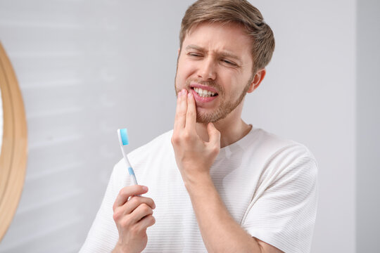 Man suffering from pain while brushing teeth in bathroom