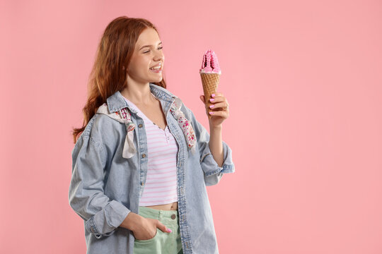 Happy teenage girl with delicious ice cream in waffle cone on pink background, space for text